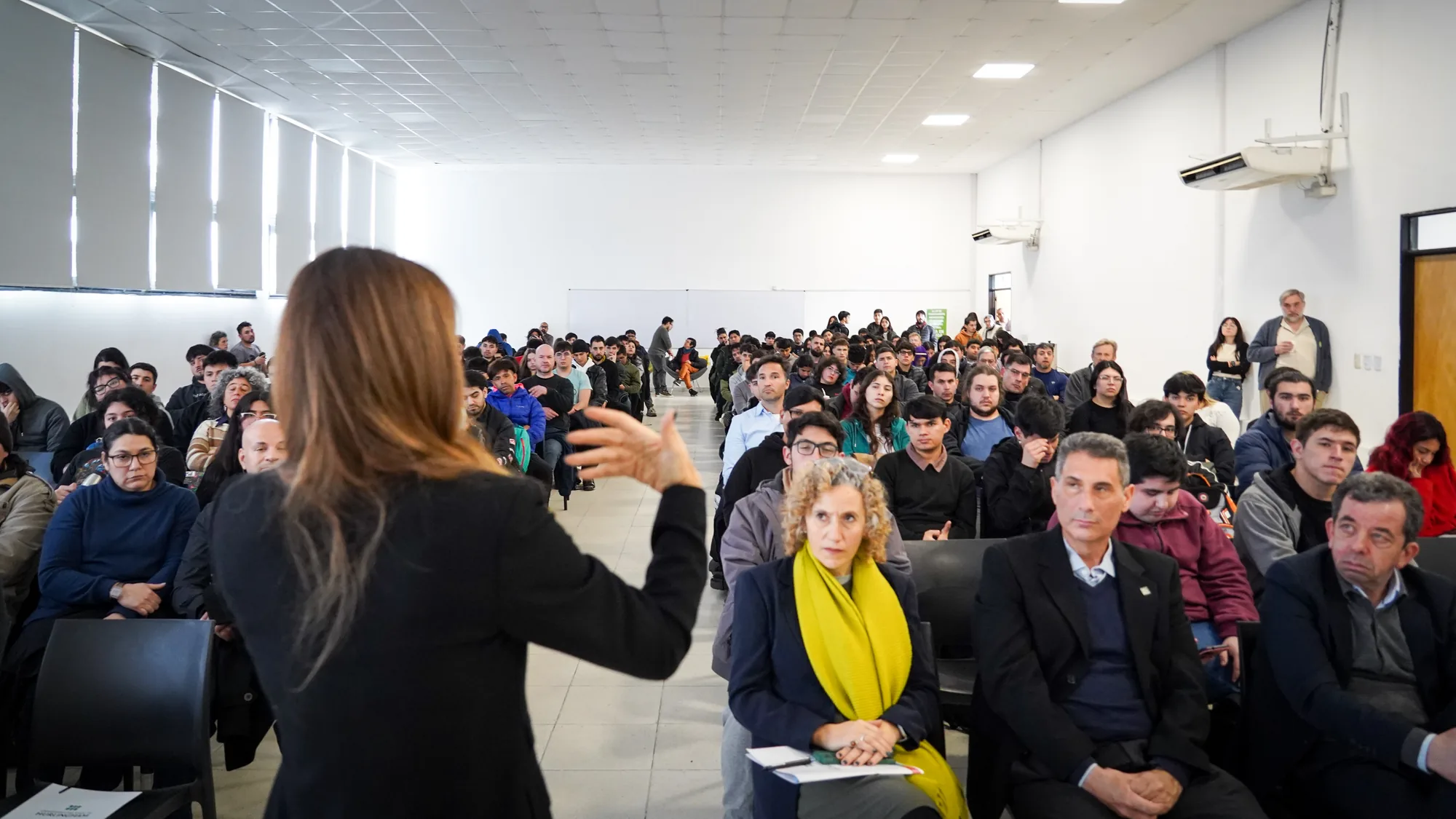 Flavia Royon, de espaldas, conversando con el público en un auditorio